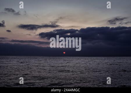 Ocean landscape with dark blue sky, calm sea and sun on the horizon. Stock Photo