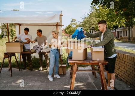 Group of male and female volunteers sorting clothes from cardboard boxes on table at community center Stock Photo