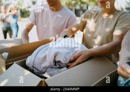 Midsection of male and female volunteers packing clothes in boxes during charity drive at community center Stock Photo