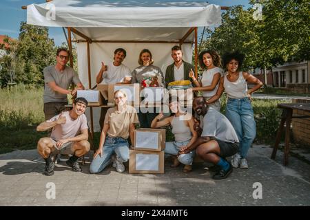 Portrait of diverse male and female volunteers showing thumbs up gesture while posing with boxes during charity drive at Stock Photo