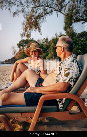 Happy senior couple having fun while sitting on deck chair at beach Stock Photo