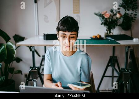 Young female freelancer talking through smart phone while using laptop at home Stock Photo