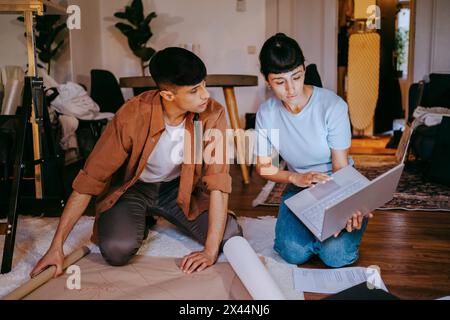 Young male and female freelancers using laptop while kneeling on floor at home office Stock Photo