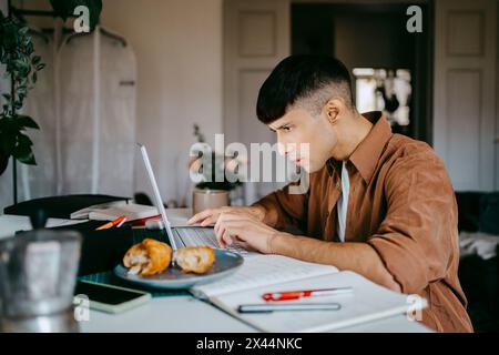 Focused male freelancer using laptop at desk while working from home Stock Photo
