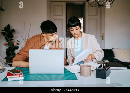 Male and female business professionals discussing over documents while sitting at desk with laptop in home office Stock Photo