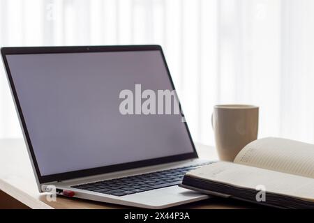 silver laptop whit blank white screen ,notebook and coffee cup nearby, at a table, image in light colors, online lesson or online meeting, cafe or off Stock Photo