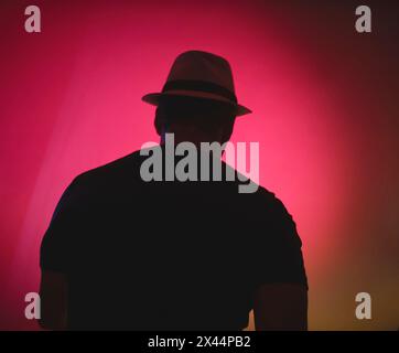 A man wearing a hat and a black shirt is standing in front of a pink background Stock Photo