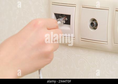 A woman's hand plugs an internet cable into an outlet, RJ-45 Stock Photo