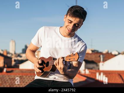 smiling man playing ukelele on a rooftop Stock Photo