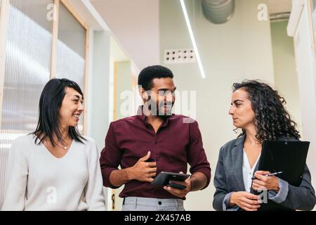 Multiracial coworkers talking happily in office corridor Stock Photo