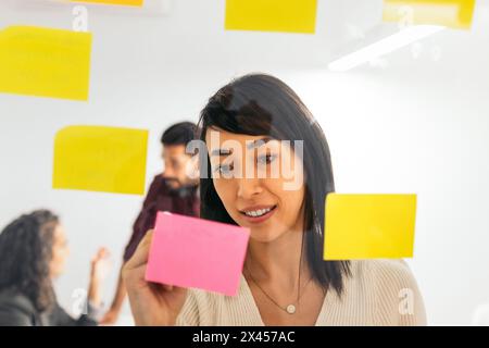 Asian woman writing on sticky notes brainstorming ideas from company meeting in coworking space Stock Photo