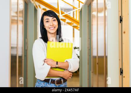 Portrait of smiling Asian woman looking at camera holding folder in modern office Stock Photo