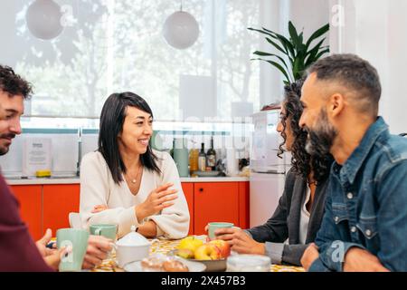 Coworkers eating happily in the kitchen of a coworking office during a break Stock Photo