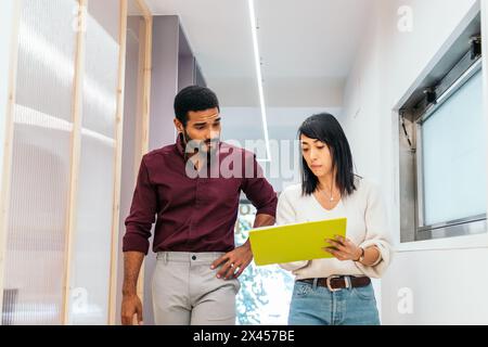 Multiracial coworkers talking reviewing and analyzing company reports in office corridor having coffee Stock Photo