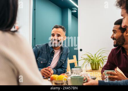 Coworkers eating happily in the kitchen of a coworking office during a break Stock Photo