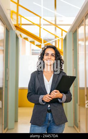 Portrait of smiling woman looking at camera holding folder in modern office Stock Photo