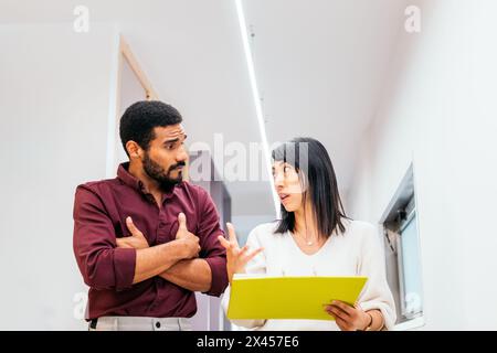 Multiracial coworkers talking reviewing and analyzing company reports in office corridor Stock Photo