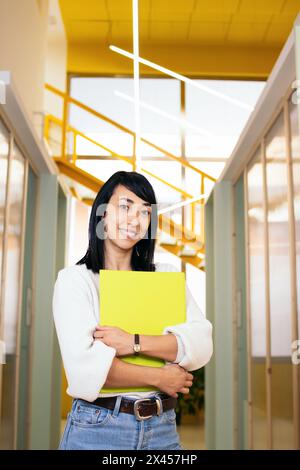 Portrait of smiling Asian woman looking at camera holding folder in modern office Stock Photo