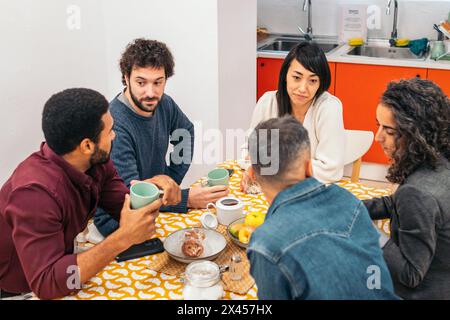 Coworkers eating happily in the kitchen of a coworking office during a break Stock Photo