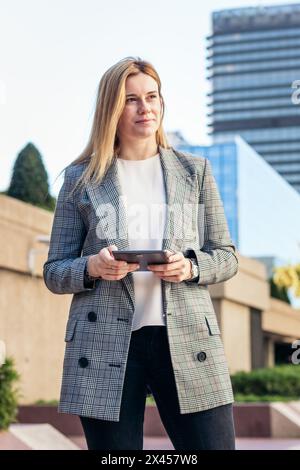 Focused blonde business woman in a suit using a tablet outside and smiling Stock Photo