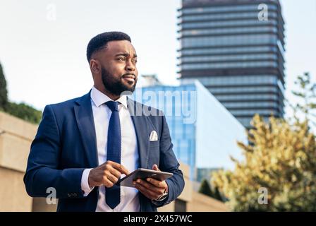 black businessman in a suit using a tablet outside. He looks concentrated Stock Photo