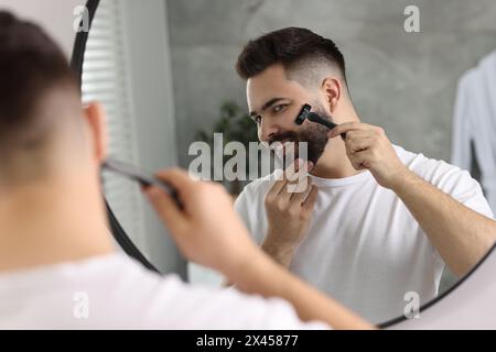 Handsome young man shaving with razor near mirror in bathroom Stock Photo