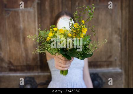 Girl or woman in front of a wooden door with a small bouquet of yellow buttercup flowers and a white peony flower Stock Photo