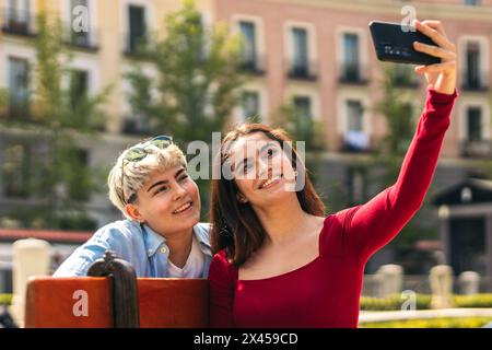 two teenager girls taking a selfie sitting on a bench Stock Photo