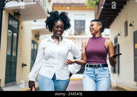 Black women stylish friends having fun walking down the street while using smartphone Stock Photo