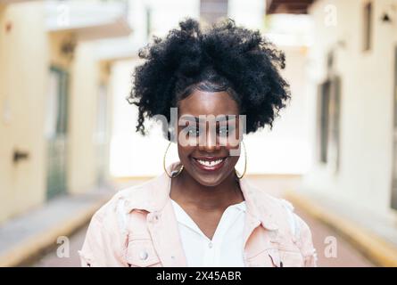 Portrait of a pretty black woman with afro hair looking at the camera. She has slightly spaced teeth and characteristic features. She looks happy. Stock Photo