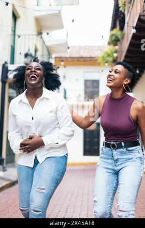 Women laughing together walking down city street Stock Photo - Alamy