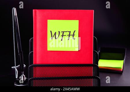 New business concept. Letters WFH, Work From Home on a yellow sticker on a red notepad in front of a black background. A place to copy Stock Photo