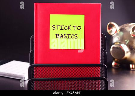 Business concept. Text STICK TO BASICS written on a yellow sticker glued to a red business notebook on a black background Stock Photo