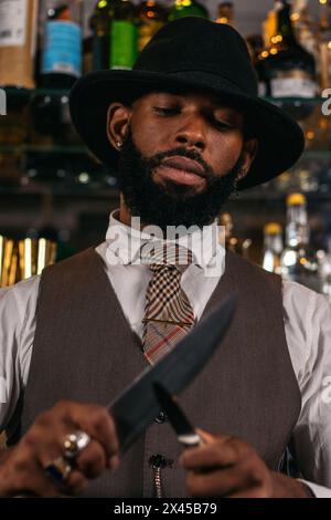 Close-up of a stylish black bartender in a hat sharpening his knives Stock Photo