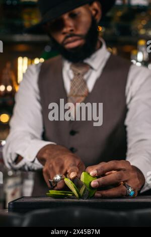 Close-up of a stylish black bartender in a hat cutting limes to prepare cocktails Stock Photo