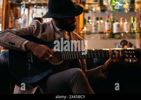 Stylish black man in hat and classic outfit playing guitar indoors Stock Photo