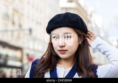 Portrait of an Asian young woman looking at camera outdoors. She has a beret and poses confidently Stock Photo