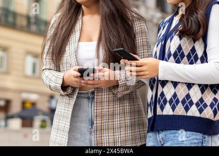 Cutout of two unrecognizable young women using smartphone in the city street Stock Photo