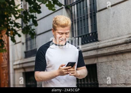 Young Albino latin man walking down the street using smartphone Stock Photo