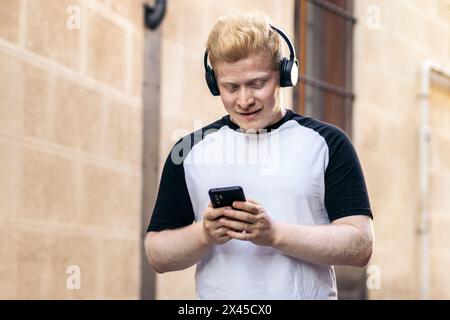 Albino man walking down the street using smartphone and listening to music with headphones Stock Photo