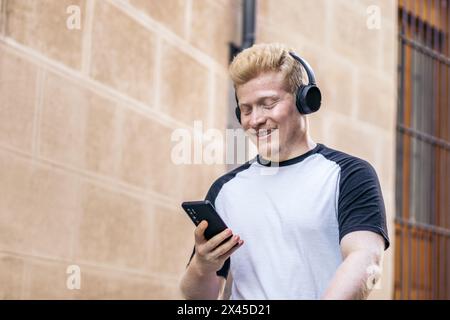 Albino man walking down the street using smartphone and listening to music with headphones Stock Photo