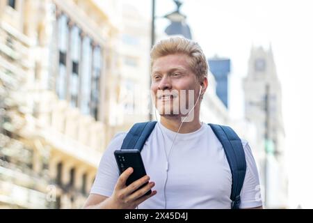 Albino man walking down the street using smartphone and listening to music with headphones Stock Photo