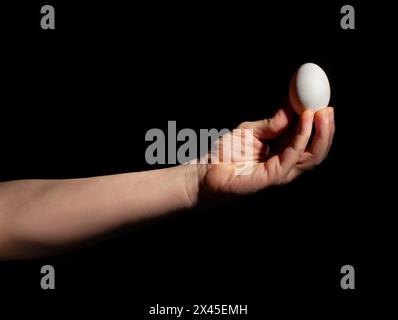 egg in hand on black background Stock Photo
