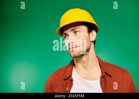 Handsome worker in uniform and hard hat stands confidently against vivid green background. Stock Photo