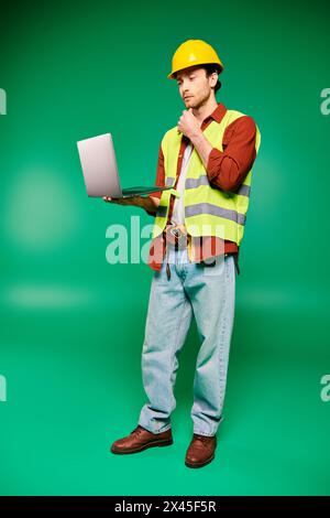 Handsome worker in hard hat holding laptop on green backdrop. Stock Photo