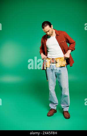 A man in uniform stands confidently holding tools against a lush green backdrop. Stock Photo