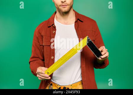 A handsome male worker in uniform holds a measuring tape on a green backdrop. Stock Photo