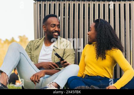 black couple sitting in a park using mobile Stock Photo