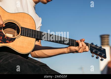 young man sitting playing acoustic guitar on a rooftop. close-up Stock Photo