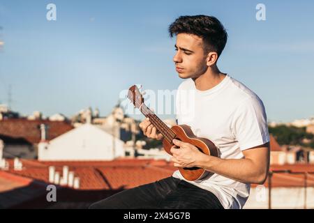 young man sitting playing ukelele on a rooftop Stock Photo